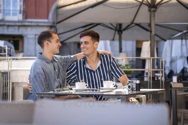 A gay couple shares a joyful moment at a charming outdoor cafe on the streets of Madrid. They are