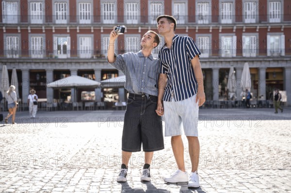 A gay couple enjoys a sunny day in Madrid, capturing memories on the bustling streets while holding