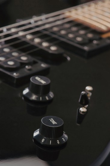 Detailed view of a black electric guitar volume and tone knobs, with strings visible. The image