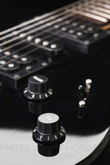 Close up image showcasing the knobs and strings of a black electric guitar, focusing on details