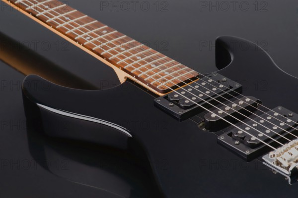 Close up shot of a sleek black electric guitar highlighting its glossy black body and warm wood