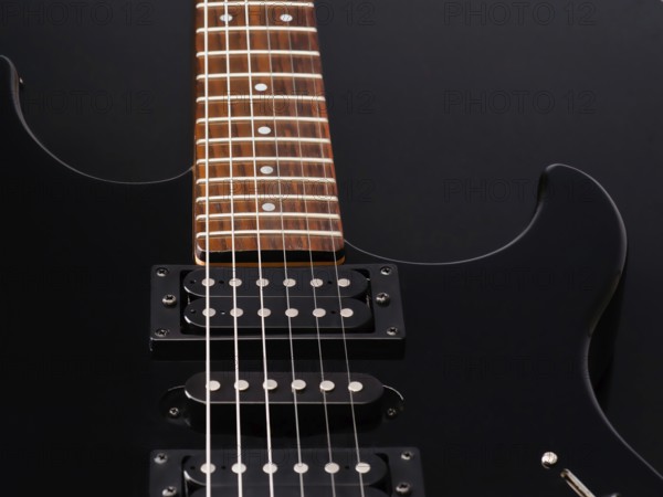 A detailed close up of a sleek black electric guitar with a wooden fretboard and shiny metal