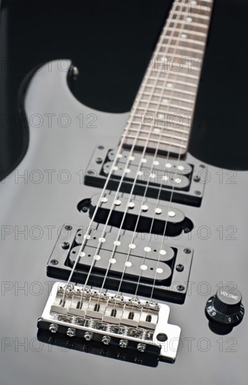 Close up image of a black electric guitar showcasing its strings, pickups, and volume knob. The