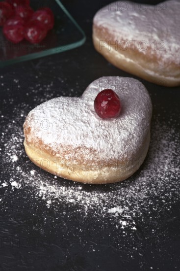 Two heart shaped cream buns, generously dusted with icing sugar and topped with a bright red