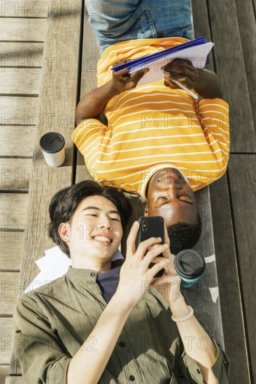 Two friends enjoy a sunny day outdoors. One is lying back with a notebook, while the other smiles