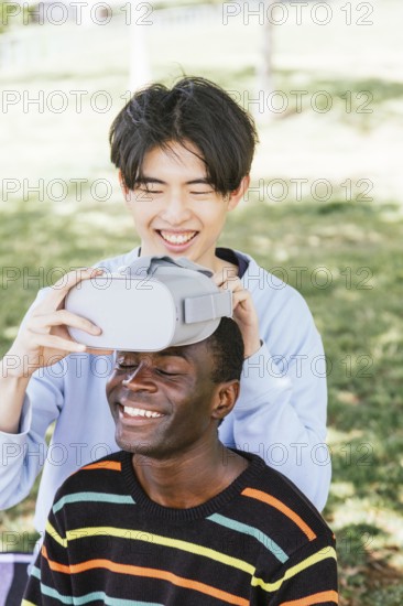 Two friends enjoying virtual reality outdoors. One adjusts the headset on the other, who smiles
