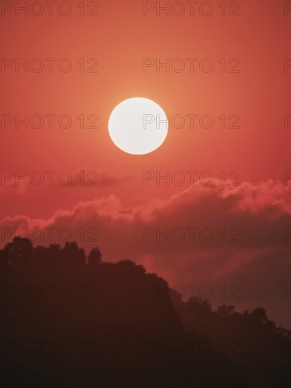 An ethereal orange sunset backlights a silhouette of mountainous terrain, expressive of untouched