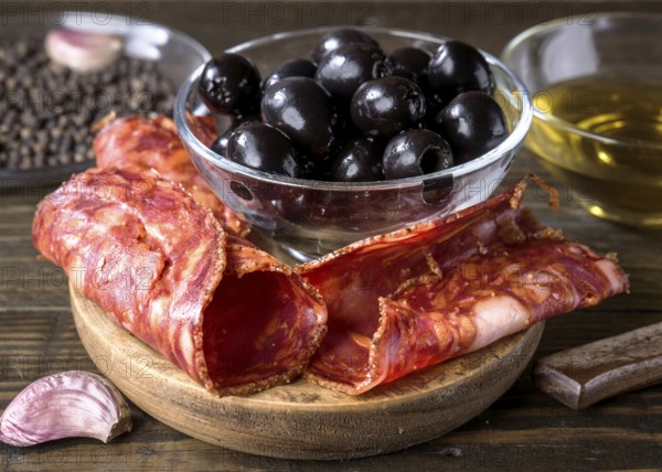A close up of a gourmet arrangement featuring spanish chorizo, black olives in a glass bowl, and a