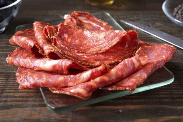 A close up shot of thinly sliced spanish chorizo arranged on a clear glass plate. The vibrant