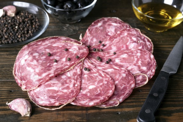 A close up view of spanish salami slices with black peppercorns on a rustic wooden table, alongside