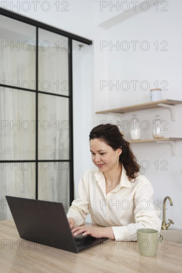 A woman works from home, sitting at a table with a laptop. She is focused and looks at the screen,