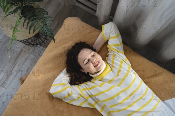 A woman lies on a brown blanket, smiling and relaxed, wearing a white and yellow striped sweater. A