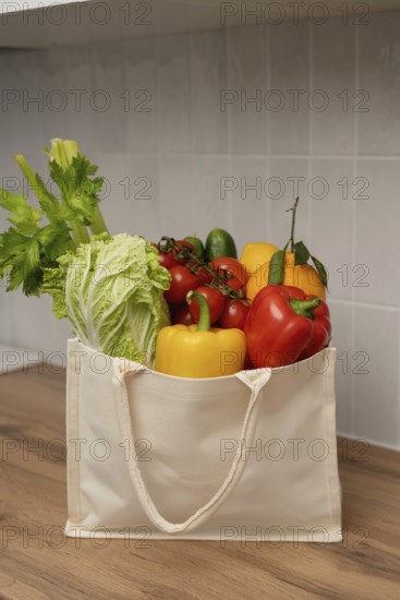 A canvas bag filled with fresh vegetables, including bell peppers, celery, and lettuce, rests on a