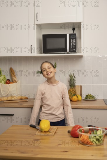A cheerful child smiles in a modern kitchen surrounded by colorful vegetables, bread, and fresh