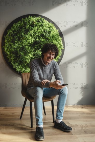 A young man with curly hair, sitting in a chair next to a vibrant green wall, embodies themes of