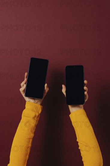 Side view of unrecognizable person in casual clothes holding smartphones with black screen while