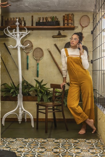 A young woman engages in teleworking, standing while using a smartphone, dressed in bold mustard