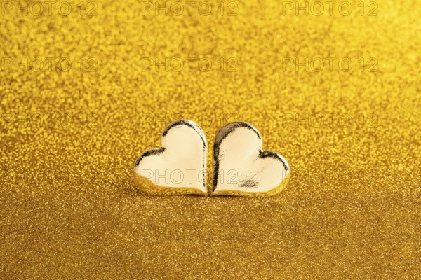 Two golden heart-shaped objects set against a shimmering golden backdrop, ideal for St. Valentine's