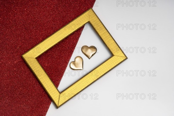 Two golden heart-shaped objects and a rectangular golden frame on a red glittery background,