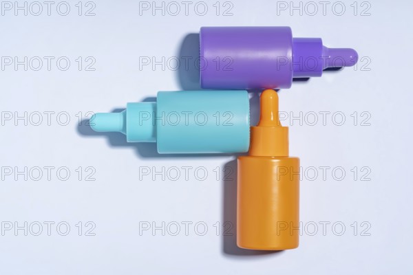 Top view of three vibrant serum bottles in purple, turquoise, and orange colors, designed with