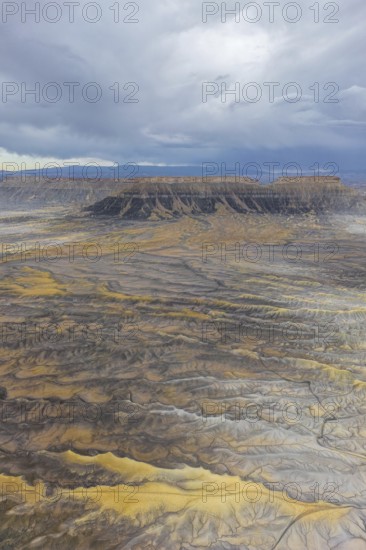 Aerial view of a rugged desert landscape featuring mesas under a cloudy sky in Hanskville, Utah.