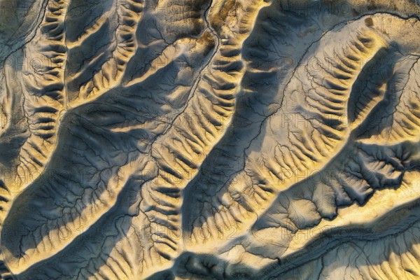 Aerial view highlighting Caineville Mesa's intricate desert patterns. Sunlight casts a warm golden