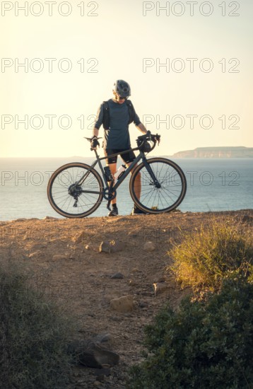 Male cyclist holding his road bike and gazing at the sea during sunset in Zahara de los Atunes,