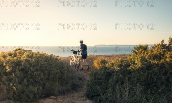 Back view of unrecognizable male cyclist standing with his bike, overlooking the ocean along a