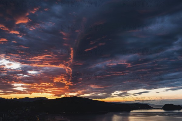 Breathtaking view of vibrant sunset skies above rolling hills framing a serene coastal backdrop,