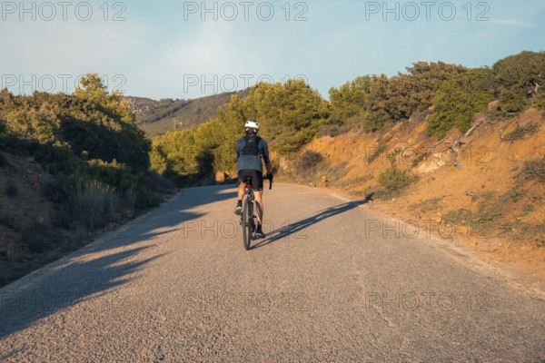 Back view of an unrecognizable male cyclist riding on a quiet road through the hills near Faro