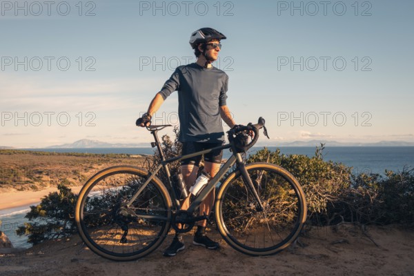 A male cyclist stands with his bike, overlooking the scenic Zahara de los Atunes, Cadiz during a