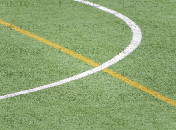 A close up of white and yellow lines marking a soccer field on artificial green turf. The detailed
