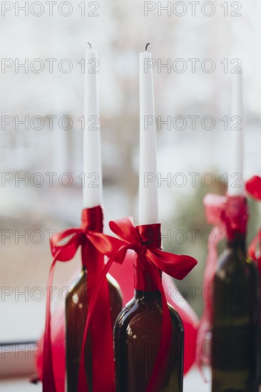 Elegant Valentine's Day decor featuring white tapered candles in wine bottles adorned with red