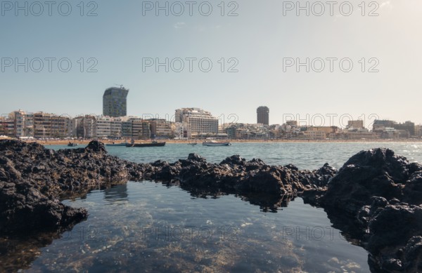 Tranquil cityscape view from volcanic rocks on a sunny day, showing modern buildings and calm