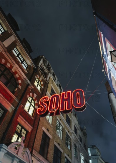 A vibrant neon Soho sign illuminates the street below, contrasting against a dark, moody London