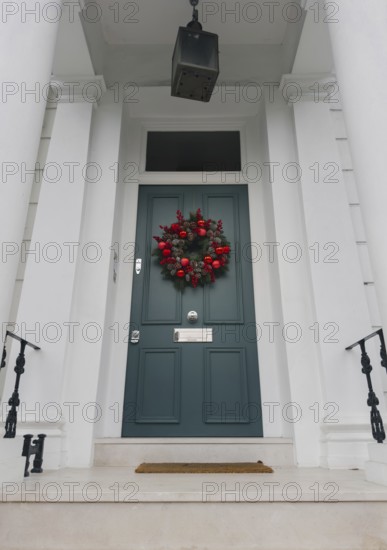 A stylish London doorway features a festive wreath with red ornaments, pinecones, and greenery