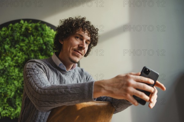 A curly-haired young man, sitting against a vivid green wall, emphasizes themes of ecology and