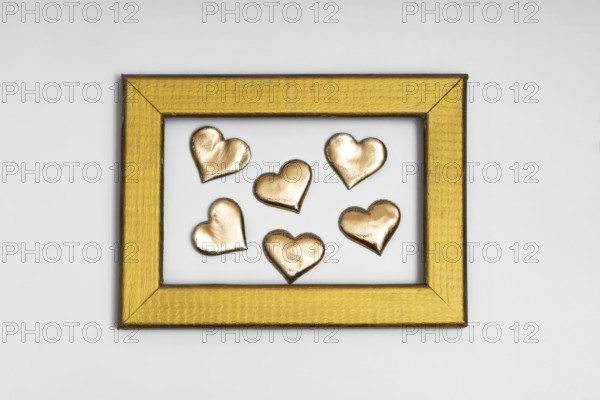 A collection of golden heart shapes arranged inside a textured gold frame, evoking themes of love