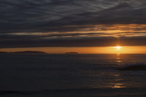 A serene sunset over the ocean, with the sun casting radiant orange and yellow hues across the sky.