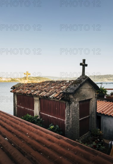 A traditional stone horreo granary with a cross atop its red tile roof overlooks a tranquil coastal