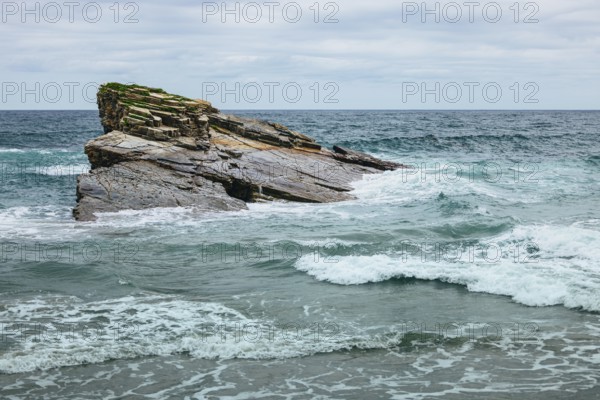 A scenic view of a rocky cliff surrounded by ocean waves crashing under a cloudy sky. The intricate