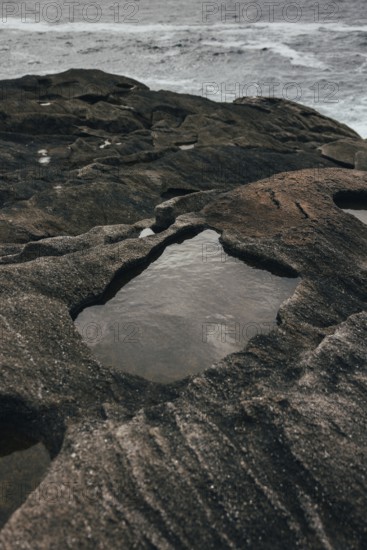 A serene coastal scene features rugged rock formations with shallow pools of water collected within