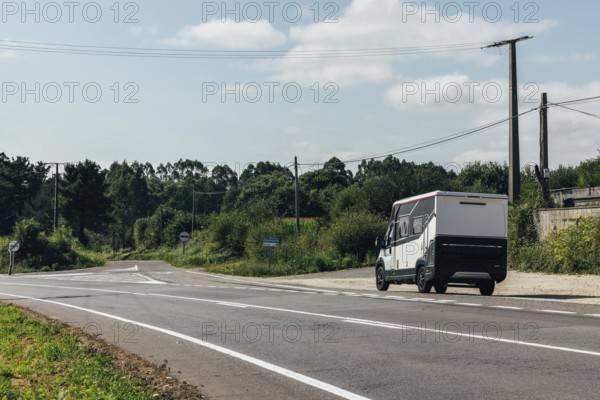 A motorhome drives on a serene rural road surrounded by lush greenery and power lines under a clear