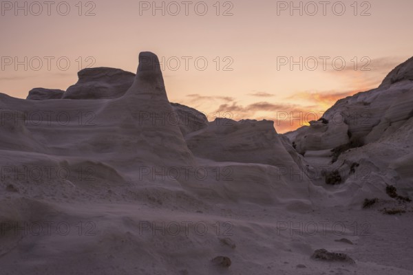 Dramatic sunset casting a warm glow over the sculptural white rock formations of Sarakiniko on the