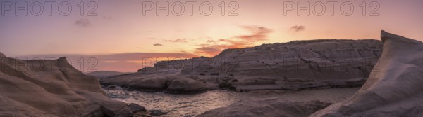 Sweeping panoramic view of Sarakiniko beach on Milos Island, Greece, under a vibrant sunset sky.