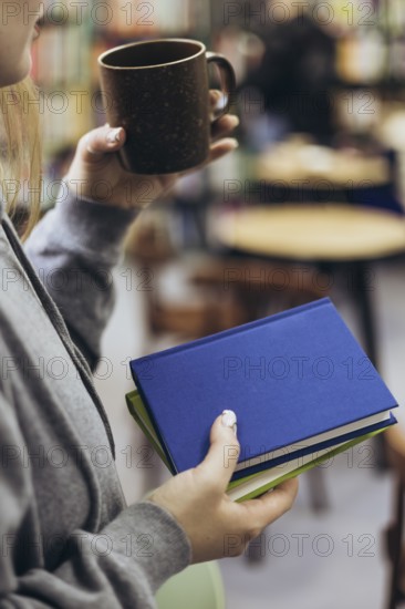 A woman in casual attire holds a coffee mug and books, enjoying a quiet moment in a cozy bookstore