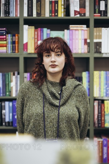 A young female academic pauses thoughtfully in a library, surrounded by colorful bookshelves filled
