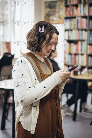 A young woman with a casual style checks her phone in a cozy bookstore. Surrounded by vibrant