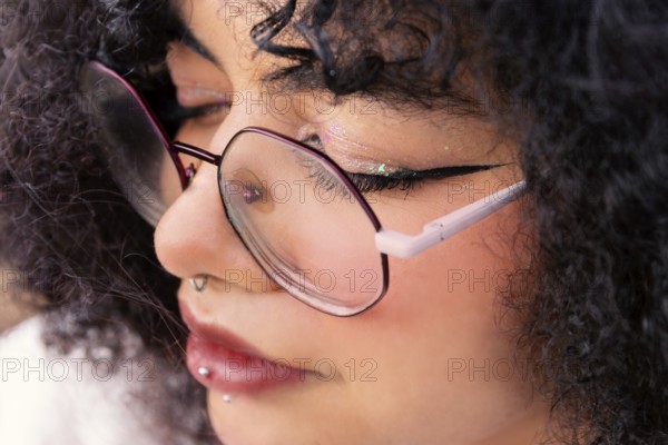 A detailed close-up shot of a latin woman wearing glasses. The focus highlights their piercings,