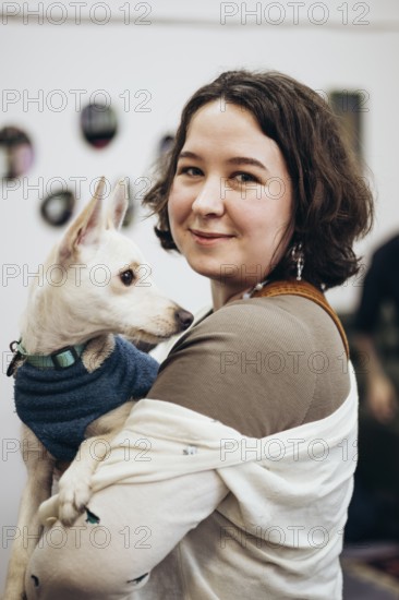 A young woman smiles warmly as she holds her adorable dog in a cozy bookstore. The pair share a